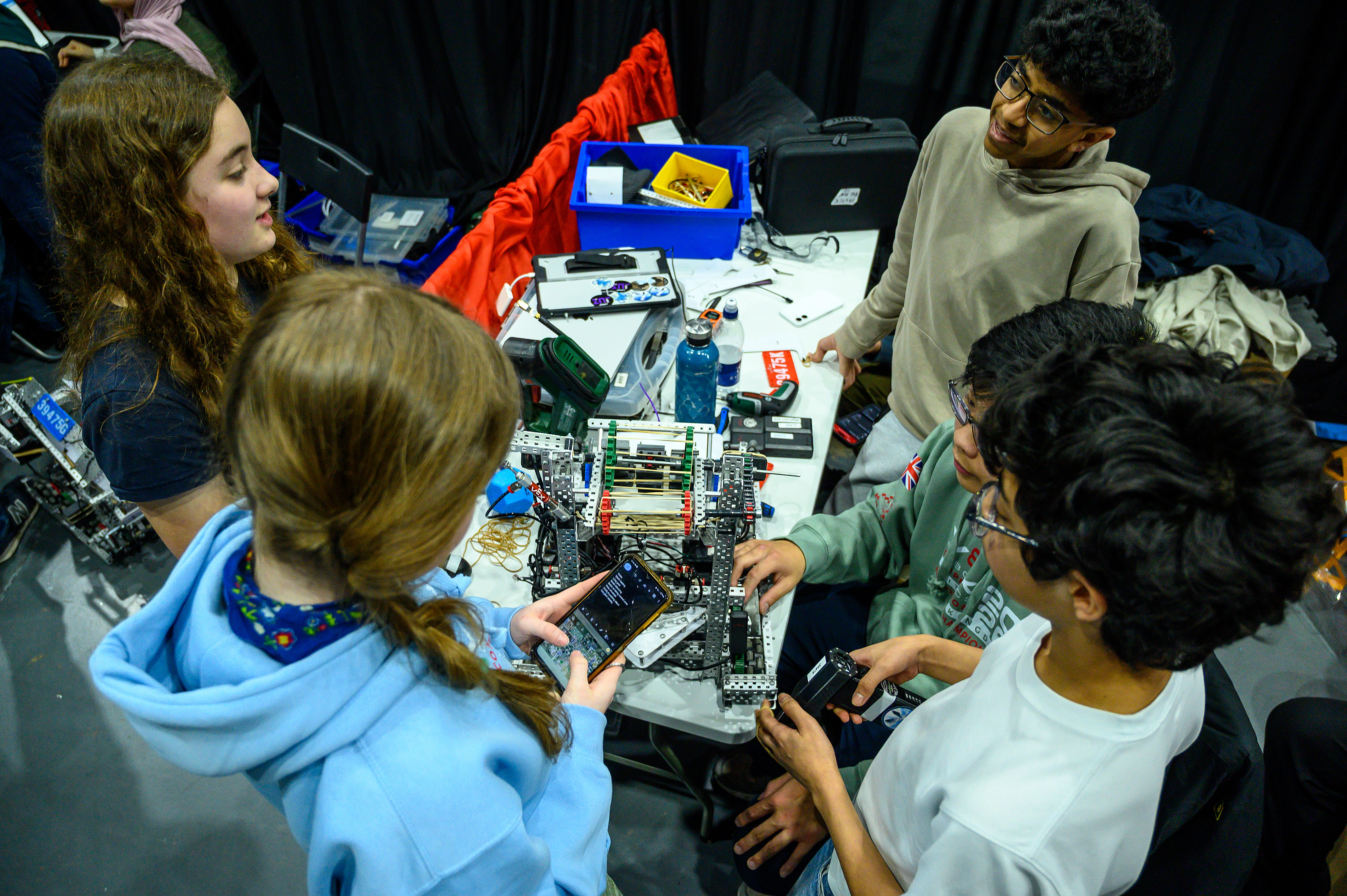 A group of students at a pit, talking over their robot together and taking notes while discussing.