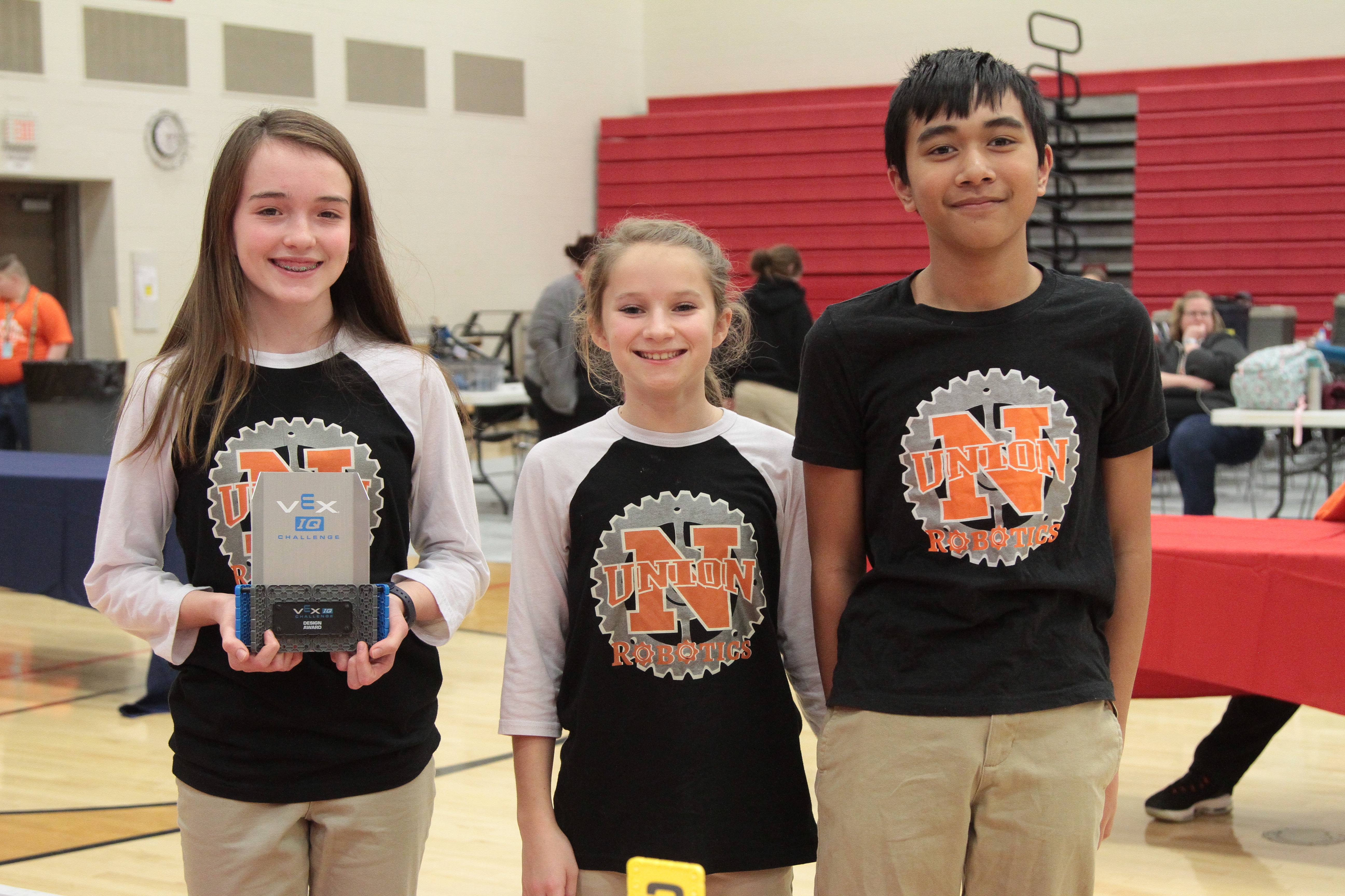Three children with one of them holding a VEX IQ Design award.