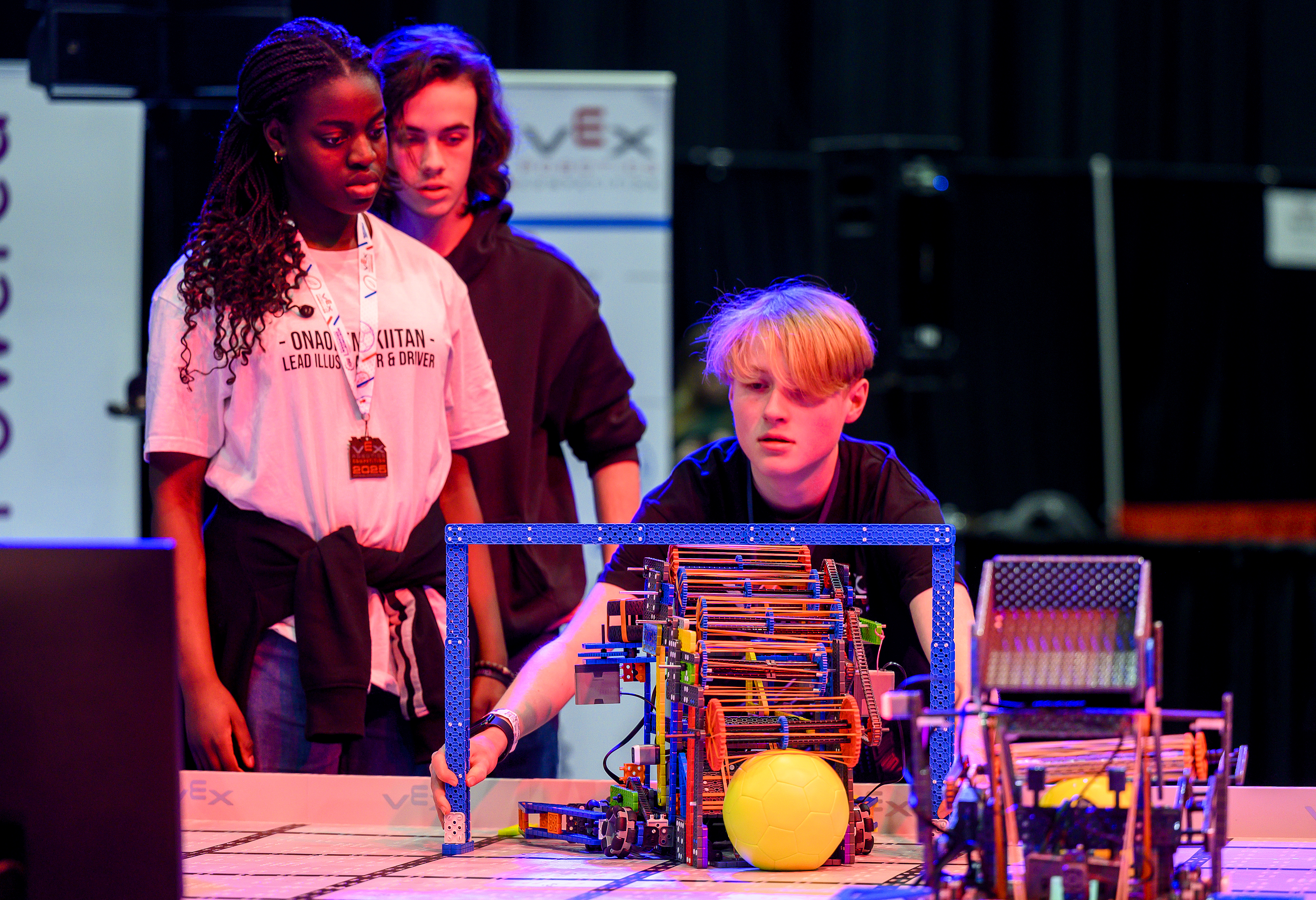 A volunteer uses the IQ sizing tool to complete the inspection process for a robot on the field, while team members look on.