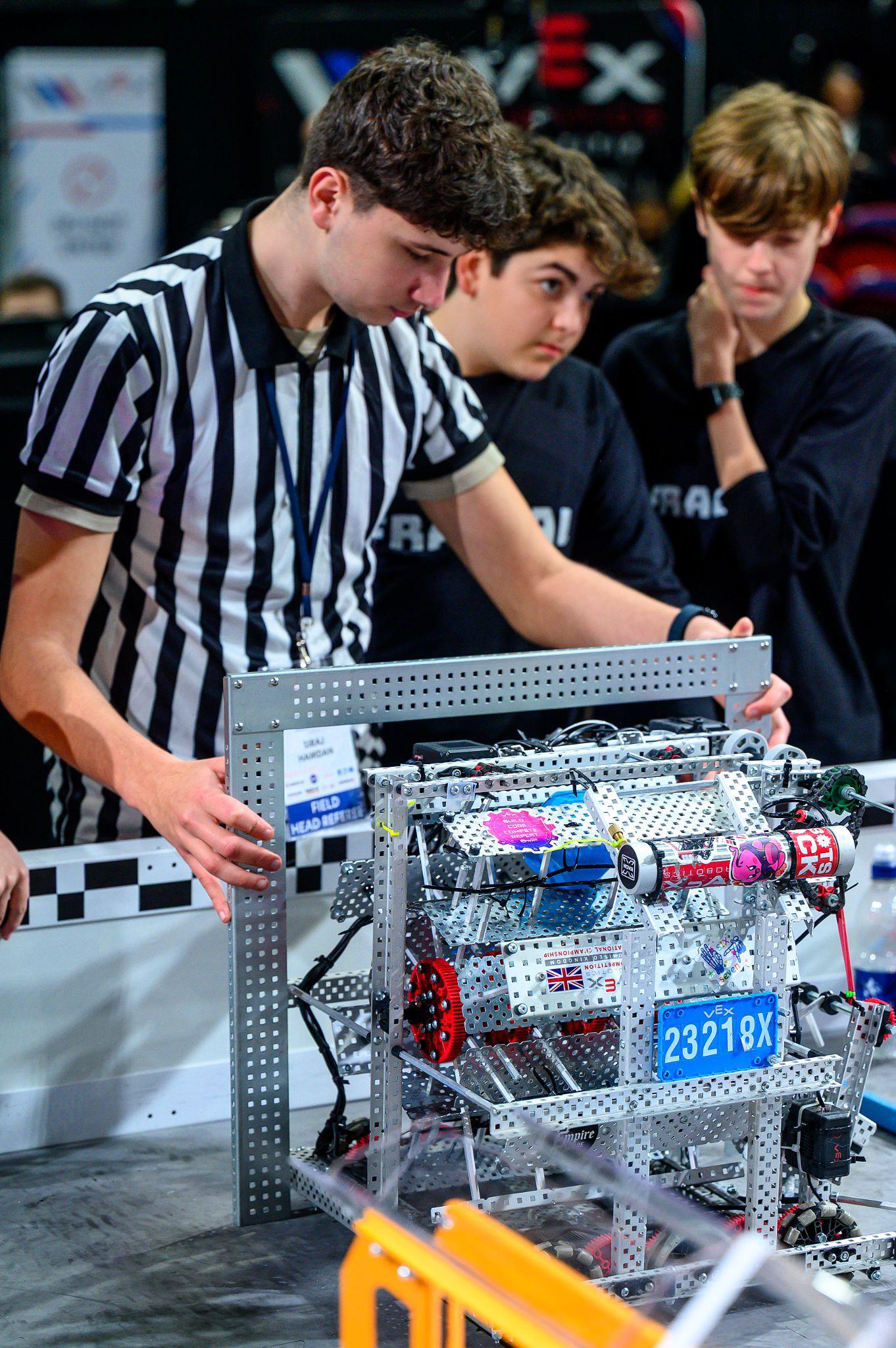 A Robot Inspector checks a team's robot while team members look on.