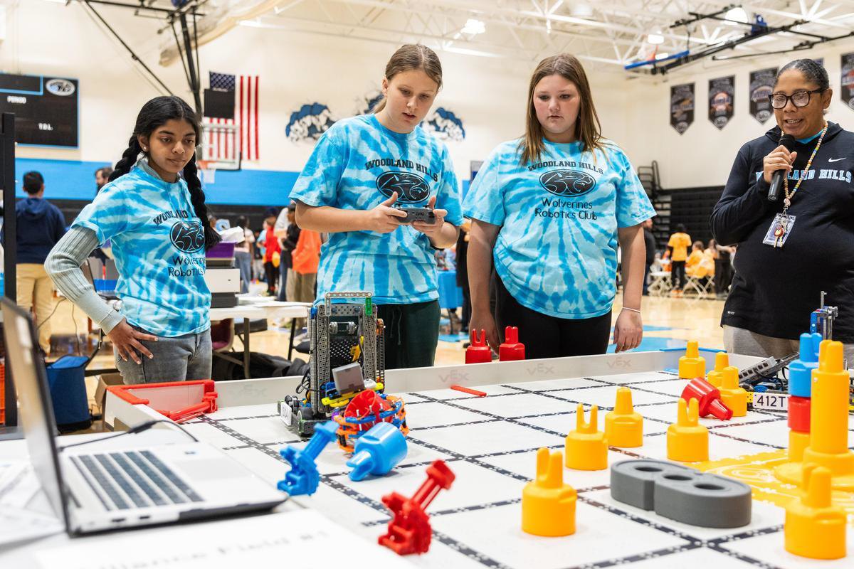An Emcee announces a match on the microphone beside a VEX IQ field.