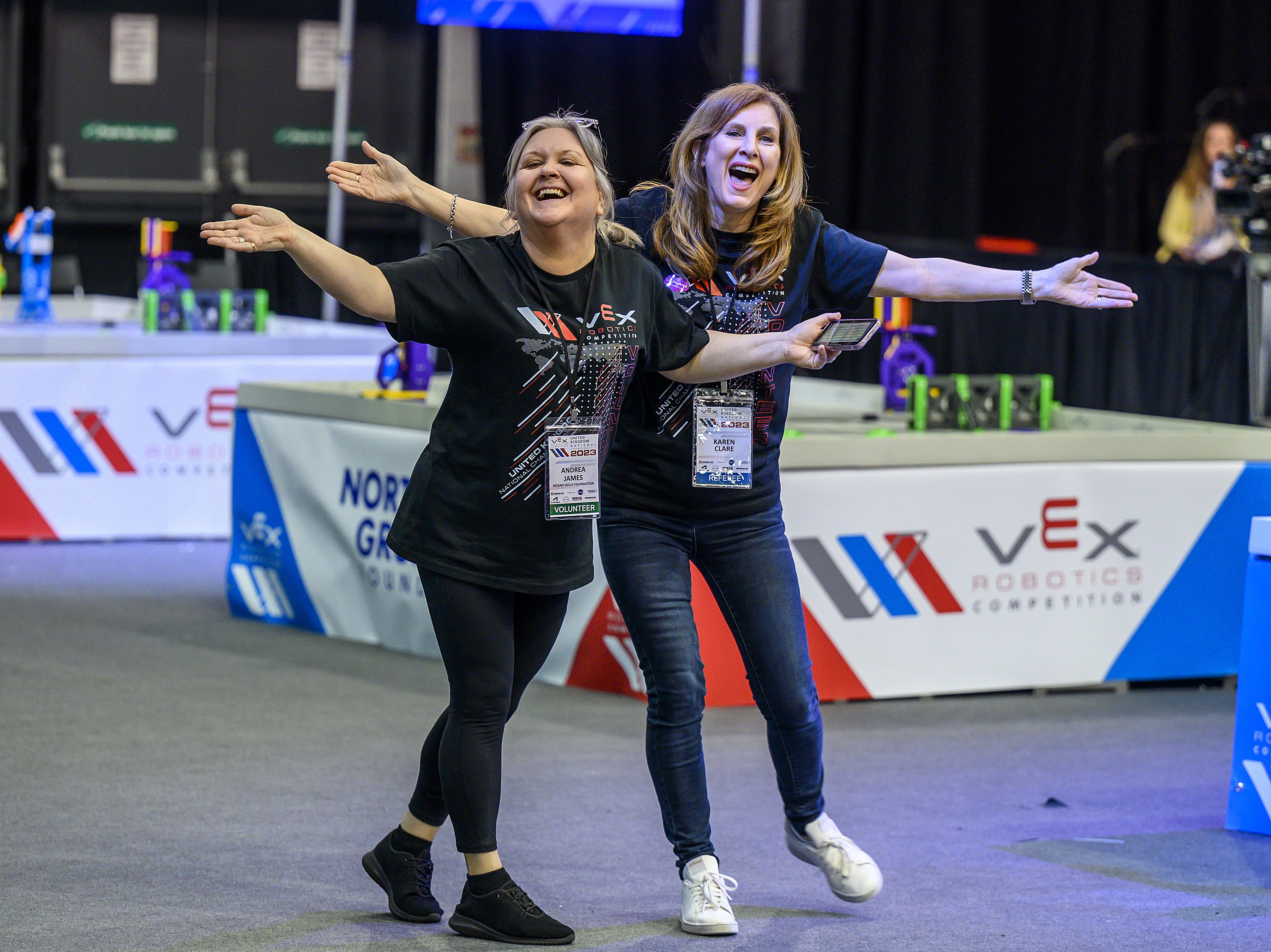 Two volunteers, one with a volunteer badge and one with a referee badge, happily smiling at the camera.