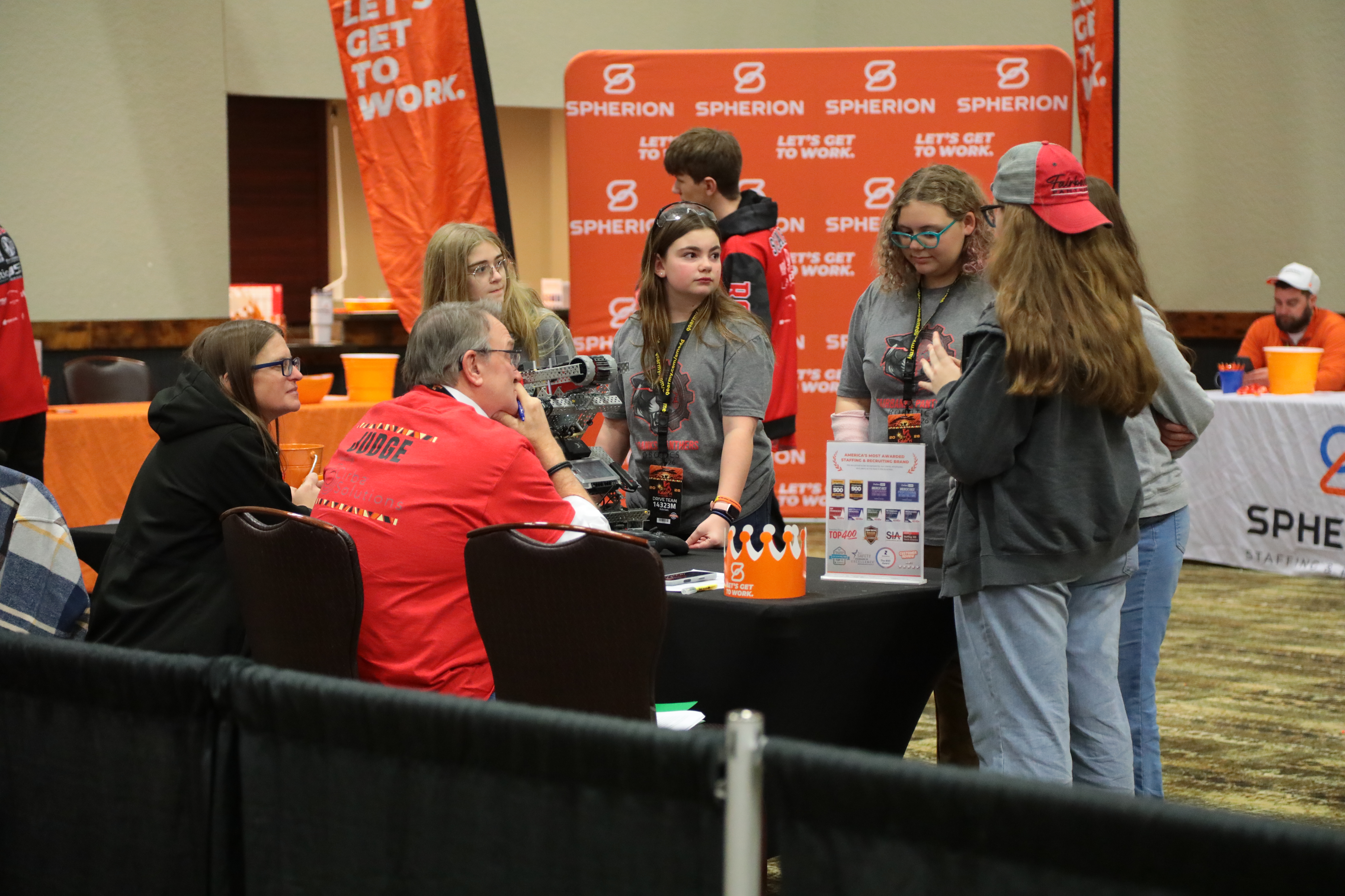 A team stands around a judge's table with their robot answering questions during a team interview. While one student talks, the rest of the team and the judges look on thoughtfully.