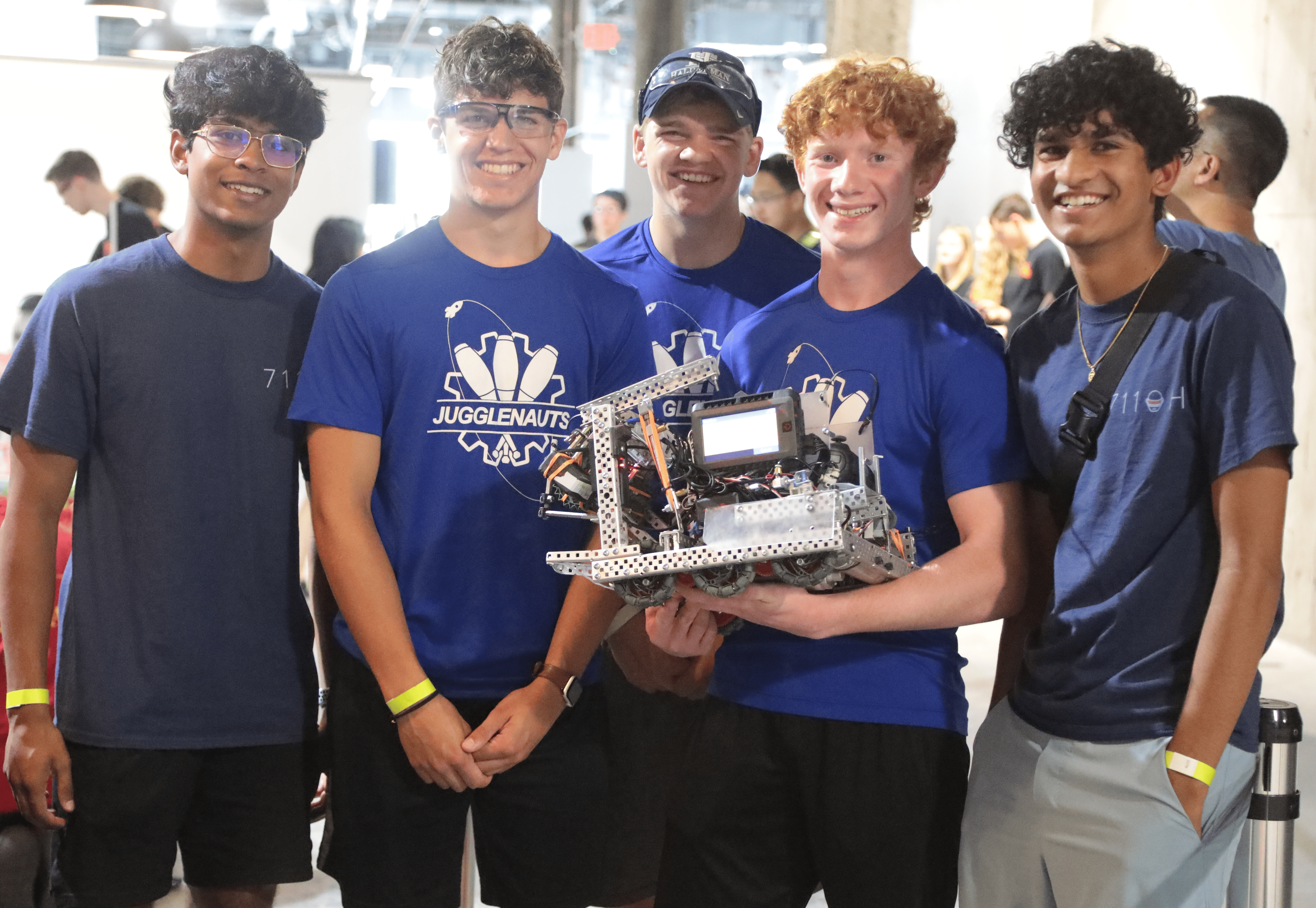A group of students holding a robot from two separate teams at a VEX Robotics competition.
